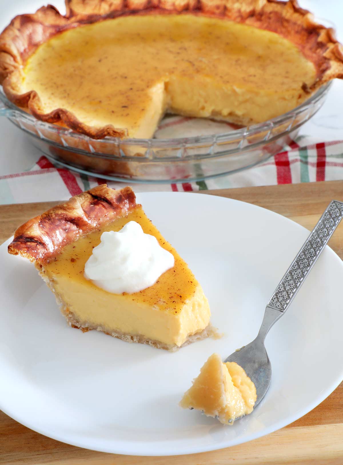 Eggnog Pie slice on a white plate topped with whipped cream with the pie plate on a kitchen counter.